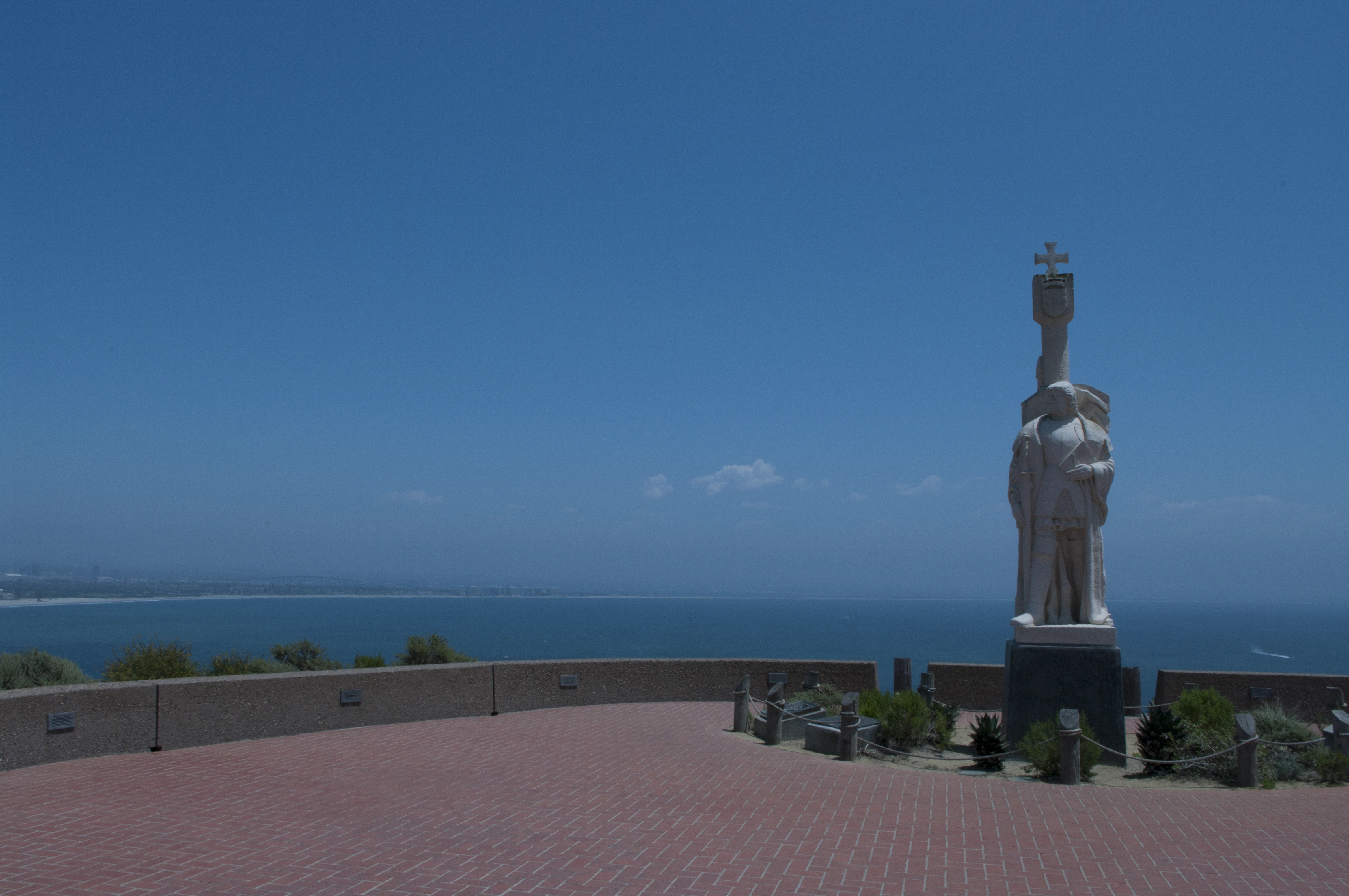 The Cabrillo National Monument statue of Juan Rodríguez Cabrillo on a wide brick plaza overlooking San Diego Bay and the Pacific Ocean under a clear blue sky